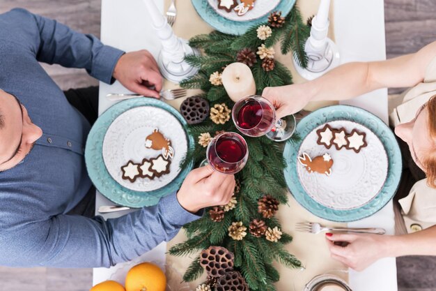 Uomo e donna tintinnio di bicchieri di vino sulla tavola di Natale con biscotti e rami di pino