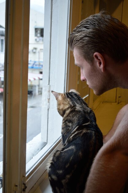 Uomo e gatto che guardano attraverso la finestra
