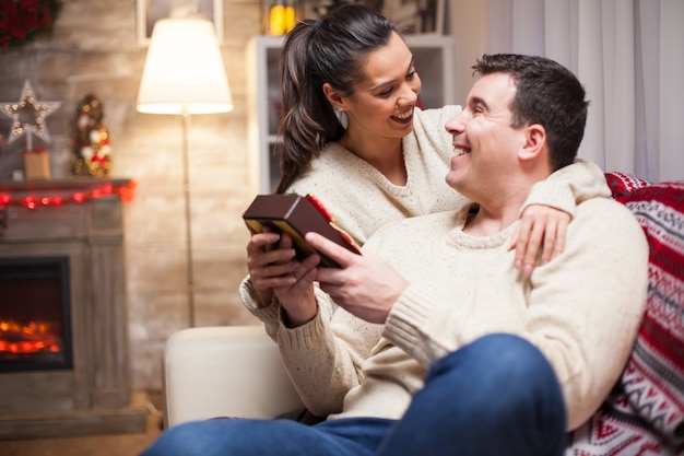 Uomo eccitato per il regalo di Natale di sua moglie seduta sul divano