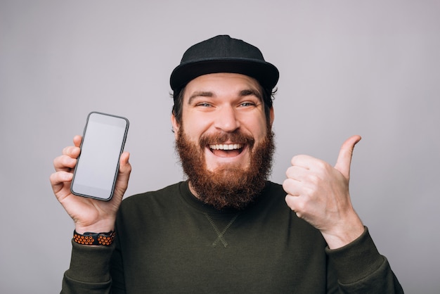 Uomo eccitato sta mostrando come gesto e il suo display del telefono.