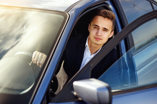 Uomo elegante bello attraente in un vestito alla guida di un'auto costosa