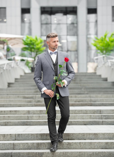 Uomo elegante in smoking Uomo che indossa un papillon in smoking All'aperto Uomo in smoking grigio con una rosa rossa