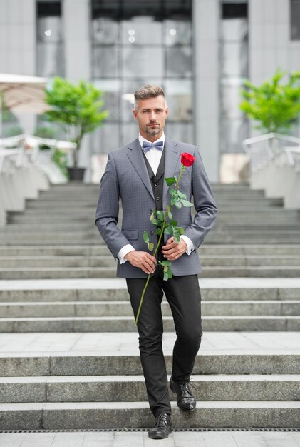 uomo elegante in smoking uomo che indossa un papillon smoking all'aperto uomo bello in smoking con rosa rossa a tutta lunghezza