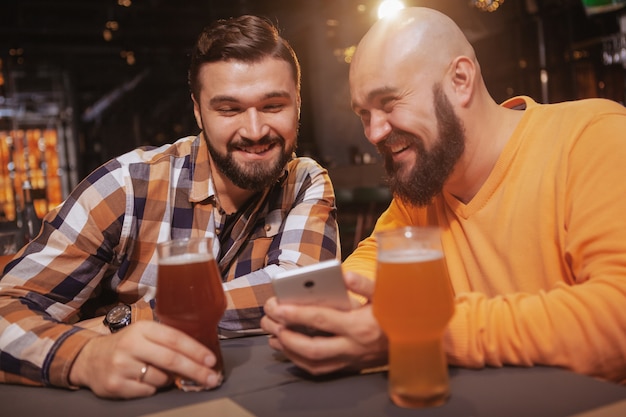 Uomo emozionante che mostra qualcosa in linea al suo amico mentre beve insieme