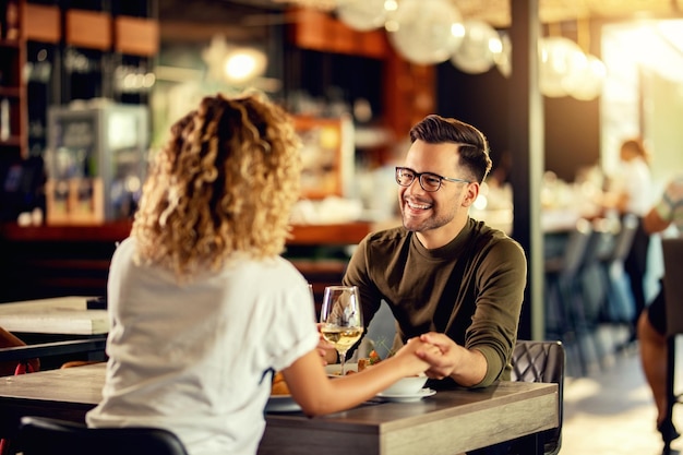 Uomo felice che comunica godendosi con la sua ragazza mentre le tiene la mano e beve vino in un ristorante