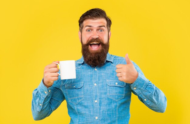 Uomo felice che dà i pollici in su tenendo lo spazio della copia del fondo giallo della tazza di caffè