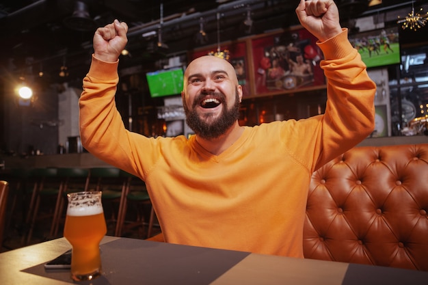 Uomo felice che grida felicemente guardando il calcio al pub della birra, celebrando la vittoria della sua squadra del cuore