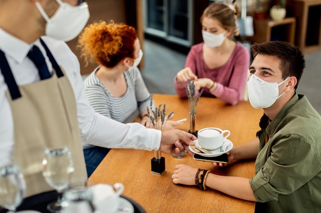 Uomo felice che indossa una maschera protettiva mentre beve caffè con gli amici in un bar