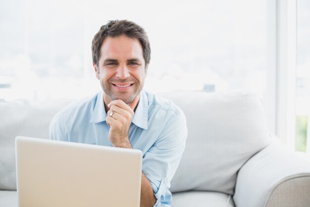 Uomo felice che per mezzo del computer portatile che sorride alla macchina fotografica