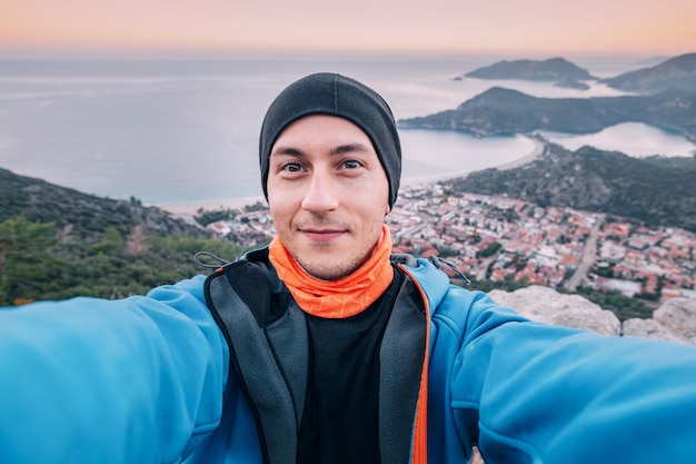 Uomo felice che prende selfie ammirando la vista di un tramonto panoramico sulla città di Oludeniz in Turchia Lycian Way attrazioni di viaggio