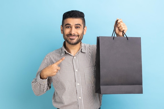 Uomo felice che punta il dito contro i sacchetti di carta in mano felice con lo shopping a prezzi bassi di buona qualità