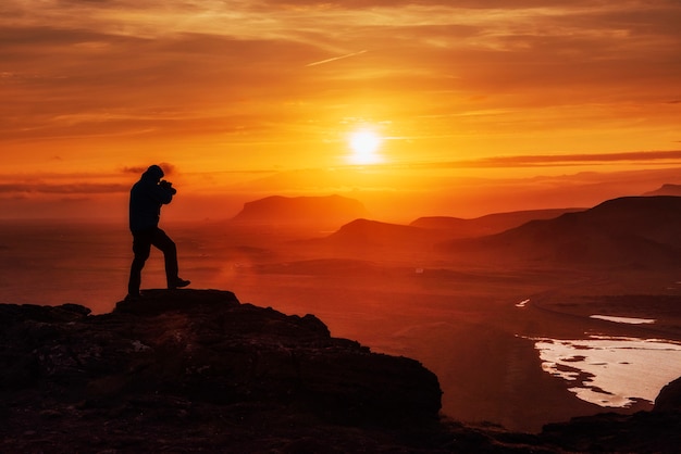 Uomo felice che sta su una scogliera al tramonto