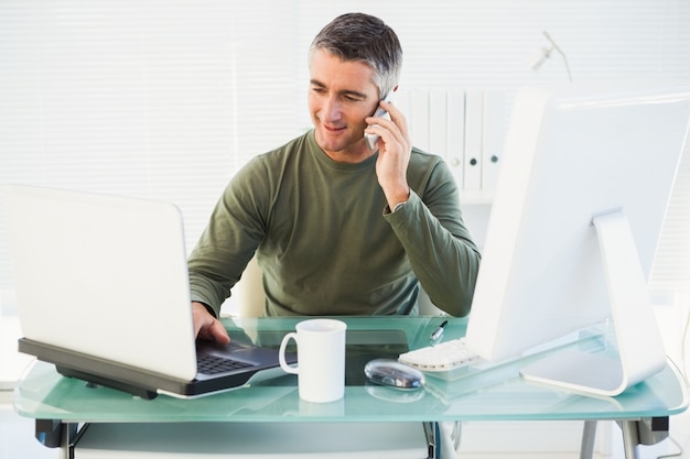 Uomo felice che telefona e che utilizza computer portatile