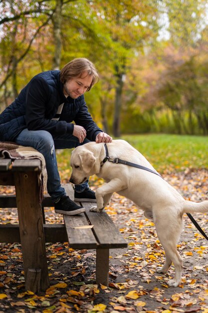 Uomo felice con il cane nel parco. Labrador annusa panchina nel parco. Concetto di migliori amici.