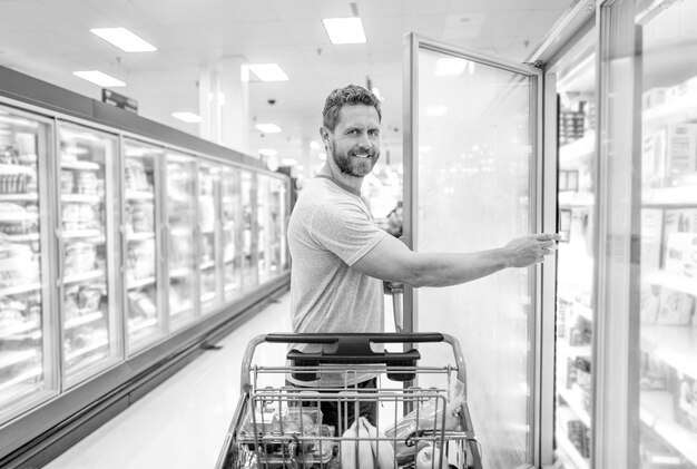 Uomo felice con il carrello che compra cibo a fare la spesa