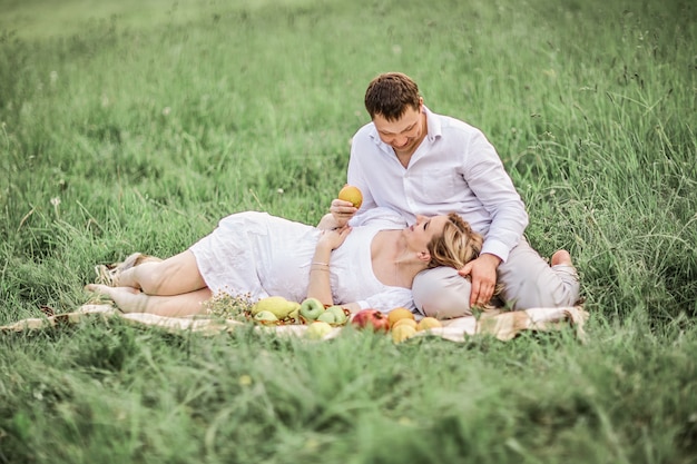 Uomo felice con la moglie incinta che riposa sul prato in una giornata estiva.