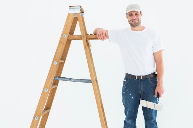 Uomo felice con la scala facente una pausa del rullo di pittura