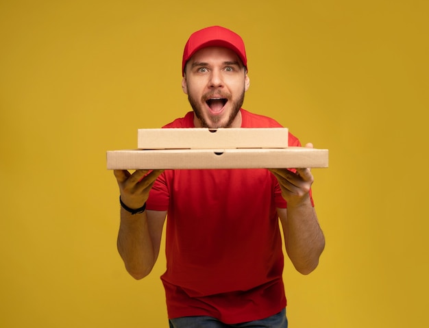 Uomo felice dal servizio di consegna in maglietta rossa e cappuccio che danno l'ordine del cibo e che tiene la scatola della pizza isolata sopra la parete gialla