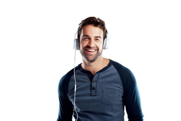 Uomo felice e cuffie per l'audio in studio su sfondo bianco per la playlist e la piattaforma di streaming Personaggio maschile ritratto e sorriso con fiducia per l'intrattenimento divertimento e godere per il suono della musica