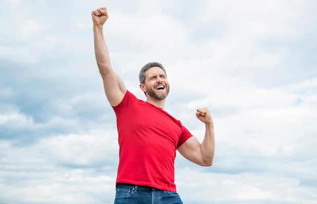 Uomo felice in camicia rossa all'aperto sulla felicità del fondo del cielo