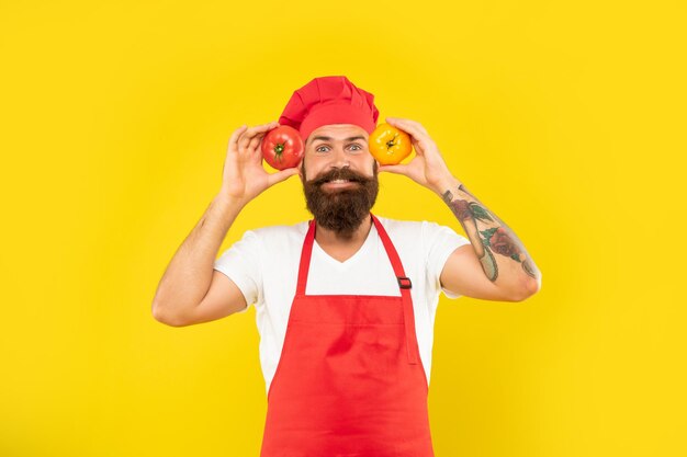 Uomo felice in grembiule da cucina e cappello che tiene i pomodori sfondo giallo chef