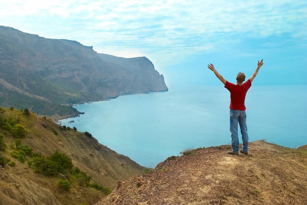 Uomo felice in piedi sulla scogliera con le mani in alto guardando il mare