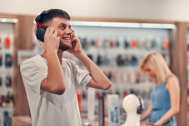 Uomo felice in posa con gli auricolari nel negozio di tecnologia. Concetto di acquisto di tecnologia.