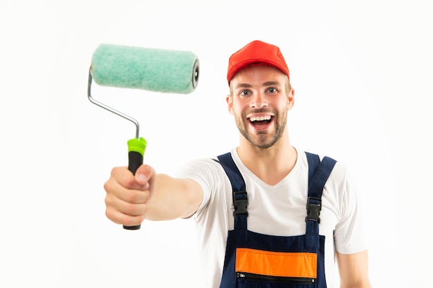 Uomo felice in rullo di vernice uniforme della tenuta del costruttore isolato sul decoratore bianco del fondo