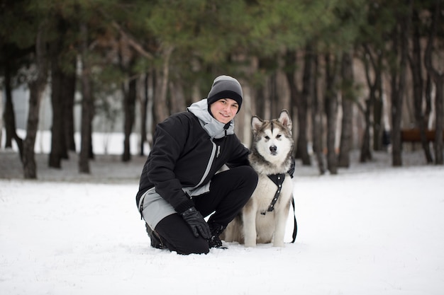 Uomo felice nella foresta invernale con un cane. Per giocare con il cane Siberian Husky.