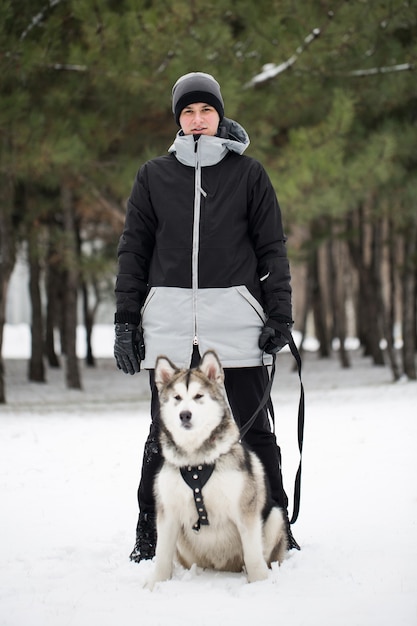 Uomo felice nella foresta invernale con un cane. Per giocare con il cane Siberian Husky.