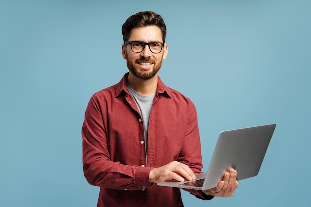 Uomo felice sorridente con gli occhiali che tiene in mano un portatile usando un computer isolato sullo sfondo blu