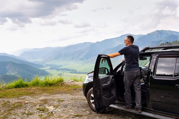 Uomo felice viaggiatore in piedi sulla sua auto in cima alle montagne.