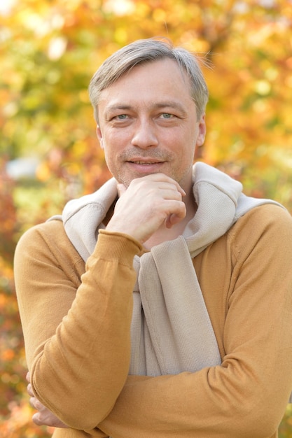 Uomo fiducioso bello che posa le foglie di autunno sullo sfondo