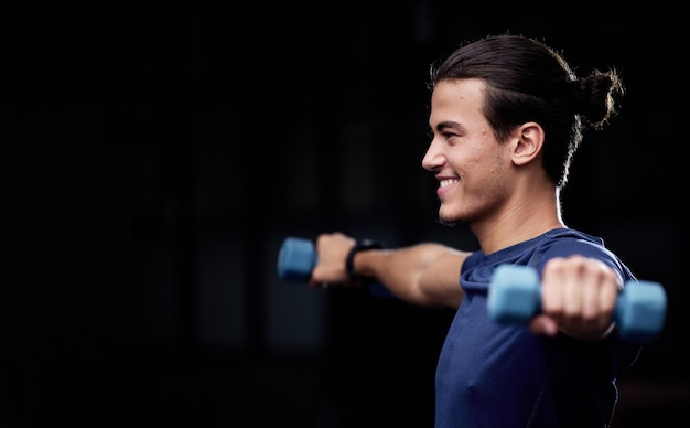 Uomo fitness e manubri con sorriso su sfondo nero per salute benessere o sviluppo muscolare Felice giovane bodybuilder sollevamento pesi o allenamento per allenamento braccia forti o esercizio in studio