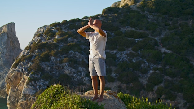 Uomo focalizzato che pratica yoga al mattino sulla bellissima scogliera dell'oceano Yogi rilassati respira