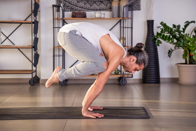 Uomo forte che esegue la postura della gru sul tappetino nello studio di yoga