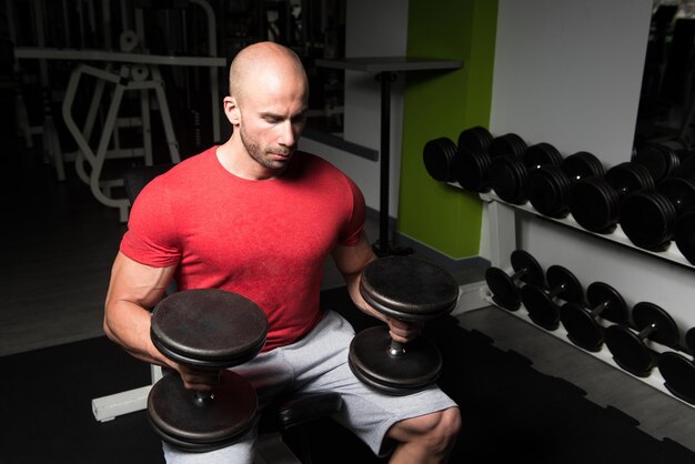 Uomo forte in palestra ed esercizio petto con manubri esercizio modello fitness bodybuilder atletico muscolare