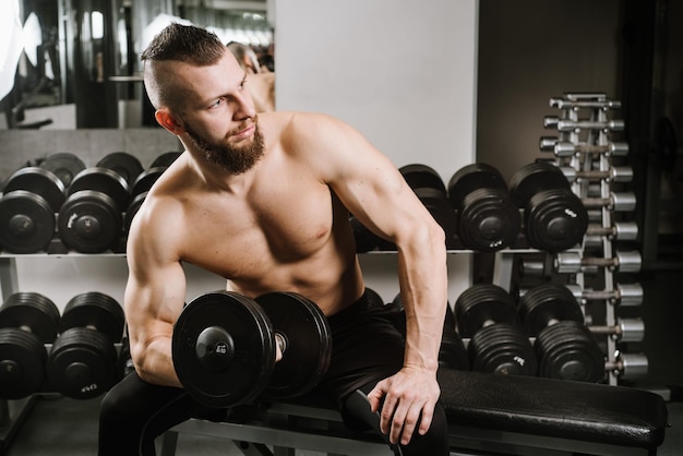 Uomo forte seduto e sollevamento manubri in palestra