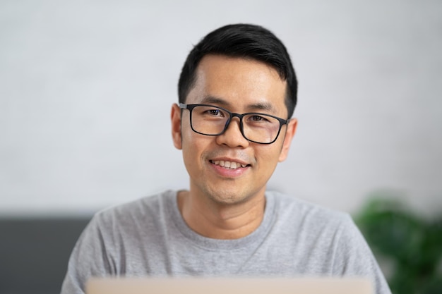 Uomo freelance in occhiali che sorride e lavora con il laptop seduto in remoto al tavolo di legno Uomo felice piacevole che comunica nei social network alla ricerca di informazioni online