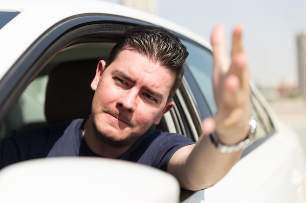 Uomo frustrato che fa un gesto attraverso la finestra mentre viaggia in macchina.