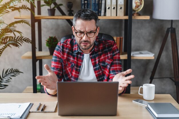 Uomo frustrato seduto alla scrivania in ufficio a casa utilizzando il computer