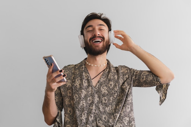 Uomo gay latino queer che guarda l'obbiettivo mentre ascolta la musica attraverso le sue cuffie su uno sfondo bianco