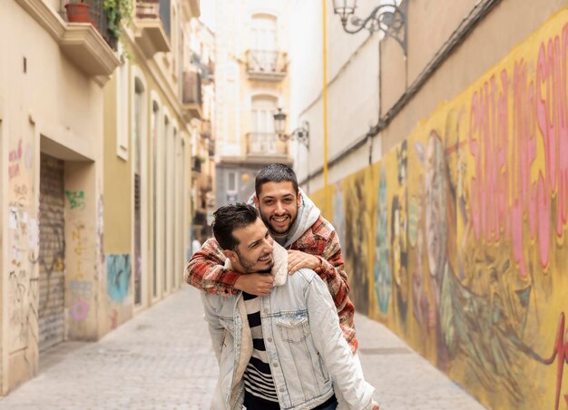 Uomo gay sorridente che trasporta sulle spalle il partner maschile mentre è per strada