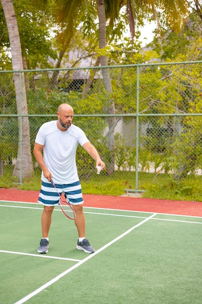 uomo gioca a badminton all'aperto all'aria fresca lancia una navetta e tiene una racchetta un'isola nelle Maldive ricreazione attiva e sport.