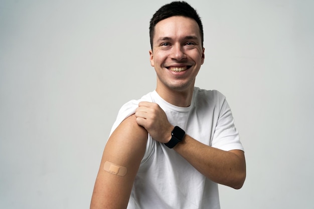 Uomo gioioso che mostra il braccio bendato dopo la vaccinazione indossando uno smartwatch che promuove la salute