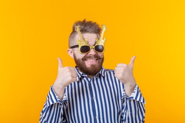 Uomo gioioso hipster alzando i pollici in posa contro un muro giallo