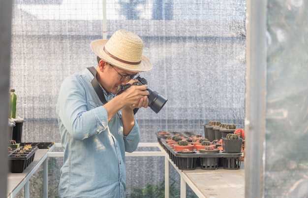 Uomo giovane agricoltore che cattura foto con la sua macchina fotografica nel giardino di cactus, concetti Hobby