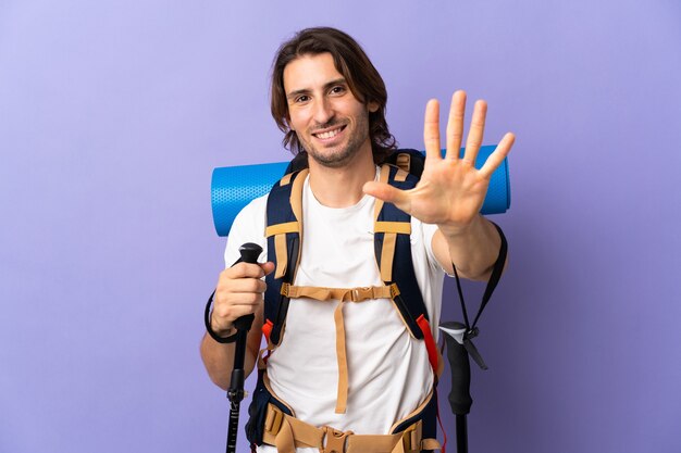 Uomo giovane alpinista con un grande zaino che conta cinque con le dita