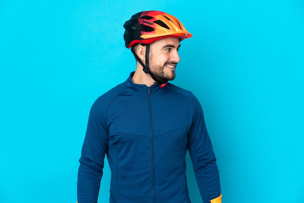 Uomo giovane ciclista isolato su sfondo blu che guarda di lato