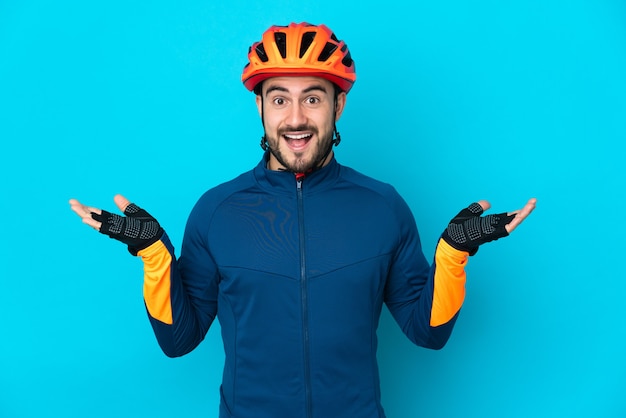 Uomo giovane ciclista isolato su sfondo blu con espressione facciale scioccata